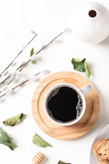 Café negro en una taza y hojas sobre una mesa blanca