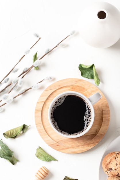 Café negro en una taza y hojas sobre una mesa blanca