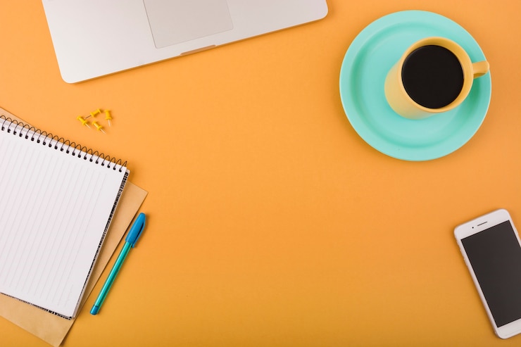 Foto gratuito café negro; teléfono inteligente; portátil y bloc de notas en el fondo naranja