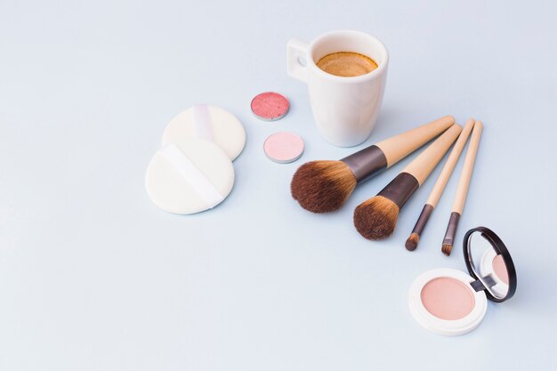 Café con pincel de maquillaje; sombra; esponja y colorete sobre fondo blanco
