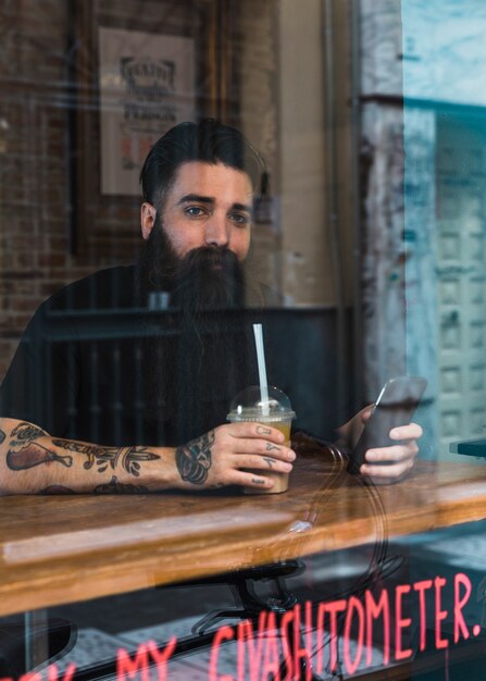 Café que se sienta empanado del hombre con el teléfono móvil y café a disposición