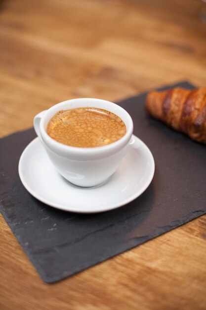 Café recién tostado en una taza blanca servido con un sabroso croissant. Aroma de café. Delicioso croissant