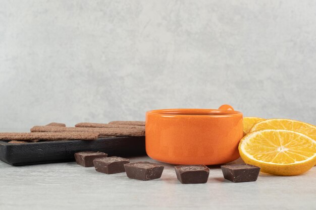 Café, rodajas de naranja, chocolate y galletas sobre superficie de mármol.