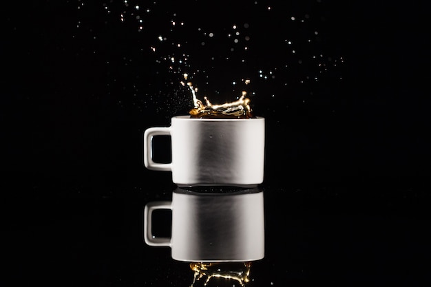 Café salpica en taza blanca sobre fondo negro