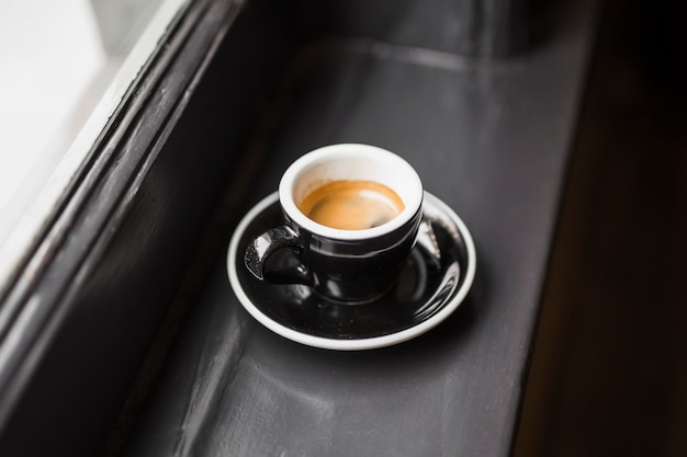 Café sobrante en taza negra en el alféizar de la ventana