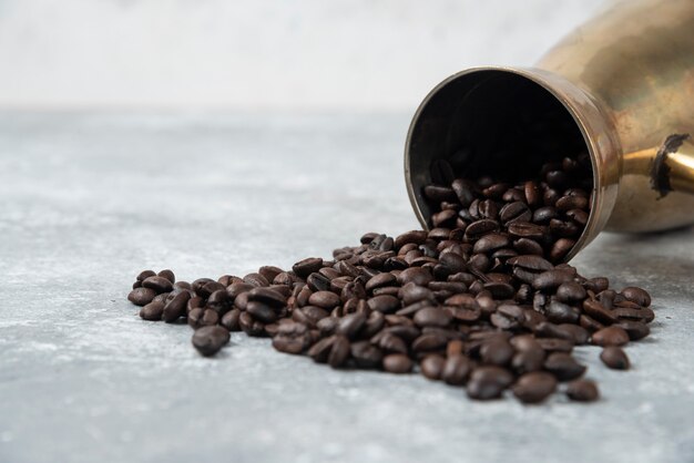 Cafetera llena de granos de café tostados sobre superficie de mármol.