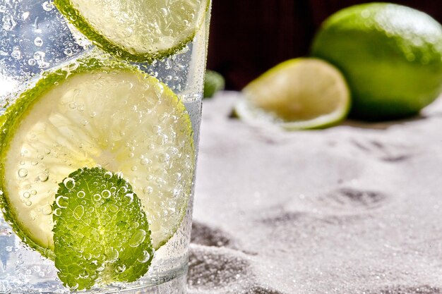 Caipirinha, cóctel Mojito, vodka o refresco con lima, menta y paja sobre fondo de arena. Naturaleza muerta. Copie el espacio. De cerca