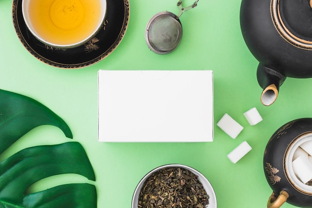 Caja blanca con té de hierbas y cubos de azúcar sobre fondo verde