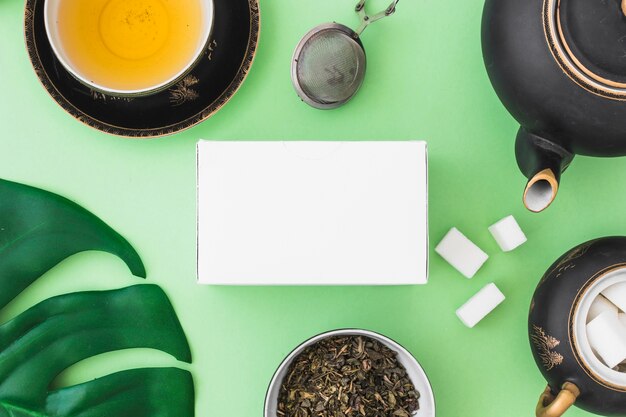 Caja blanca con té de hierbas y cubos de azúcar sobre fondo verde