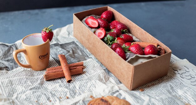 Caja de cartón de fresa con taza y canela en un periódico.