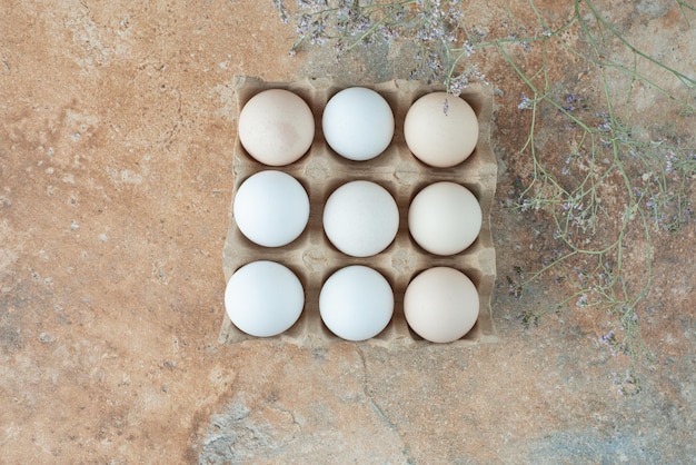 Caja de cartón con huevos blancos frescos de pollo en mesa de mármol.