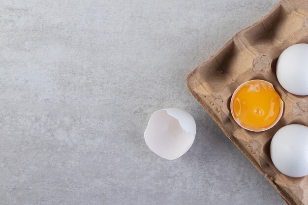 Caja de cartón de huevos crudos blancos sobre mesa de piedra.