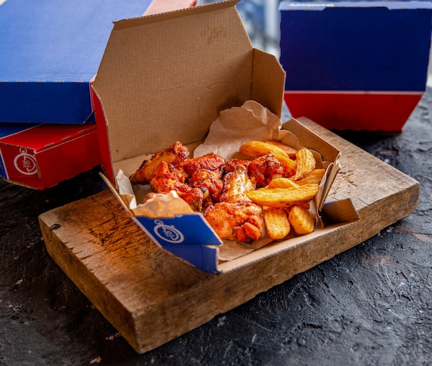 Una caja de comida para llevar con barbacoa de pollo y papas fritas dentro