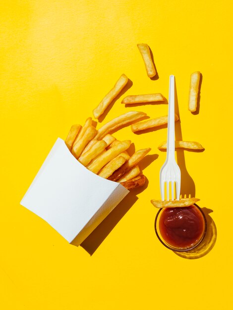 Caja derramada de papas fritas con salsa de tomate y tenedor