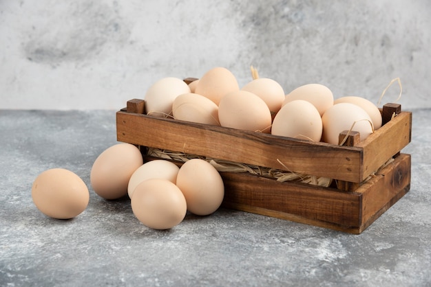 Caja de madera de huevos crudos orgánicos sobre superficie de mármol.