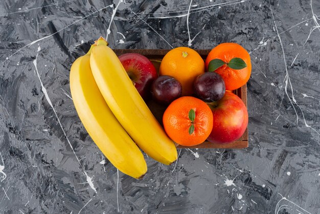 Caja de madera llena de frutas frescas sobre la superficie de mármol.