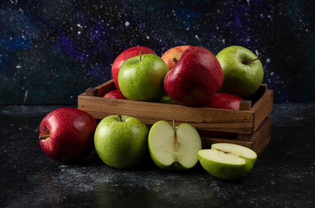 Caja de madera de manzanas orgánicas maduras sobre superficie negra. .