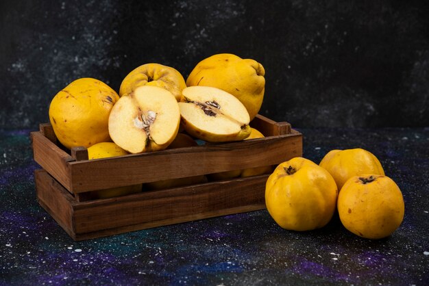 Caja de madera de membrillos maduros frescos en la mesa oscura.