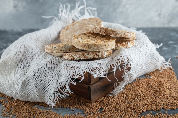 Caja de madera de pan crujiente aireado y trigo sarraceno crudo sobre superficie de mármol