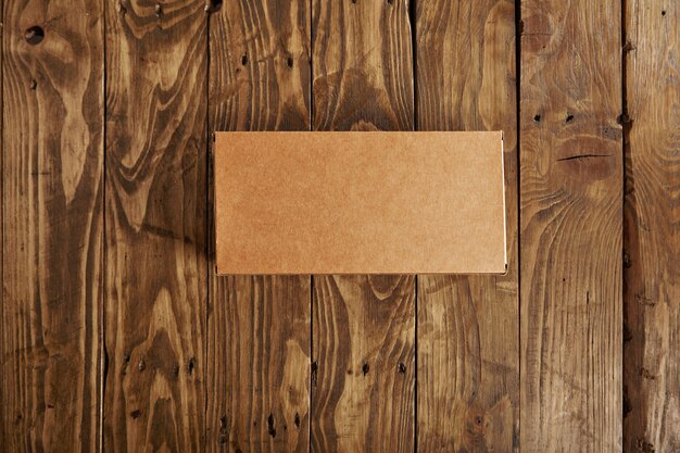 Caja de paquete de cartón en blanco artesanal presentada en mesa de madera cepillada estresada, vista superior
