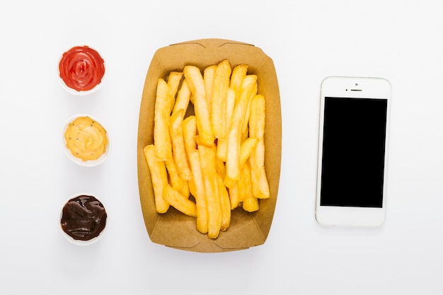 Caja plana de papas fritas con salsas y maqueta de smartphone.