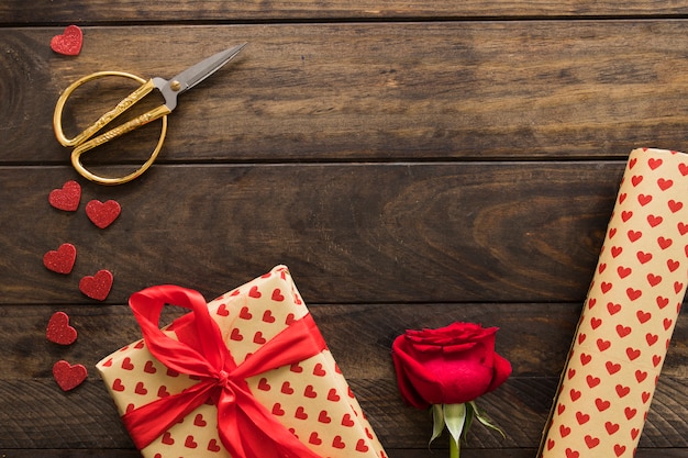 Caja de regalo cerca de rollo de papel cariño, tijeras y floración.