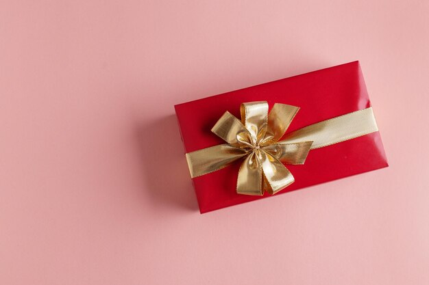 Caja de regalo con cinta dorada sobre fondo rosa.