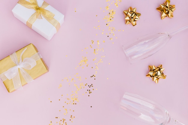 Caja de regalo envuelta con lazo; confeti dorado Gafas de arco y champagne sobre fondo rosa