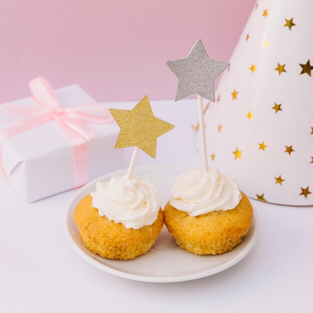 Caja de regalo envuelta; Sombrero de fiesta y cupcake con estrella dorada y plateada en escritorio blanco