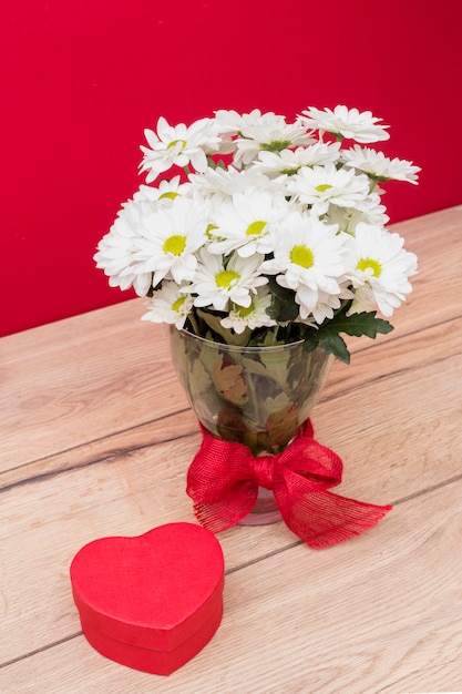 Caja de regalo en forma de corazón con ramo de flores en florero.