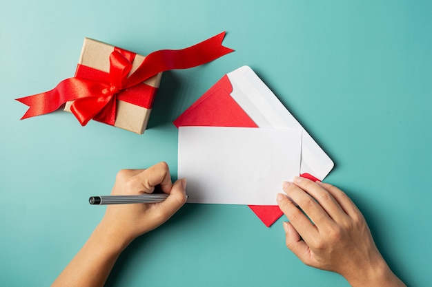 Una caja de regalo junto a la mano de la mujer está escribiendo una tarjeta de felicitación.