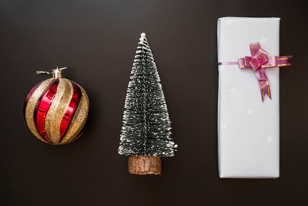 Caja de regalo con lazo cerca de bola decorativa y abeto.