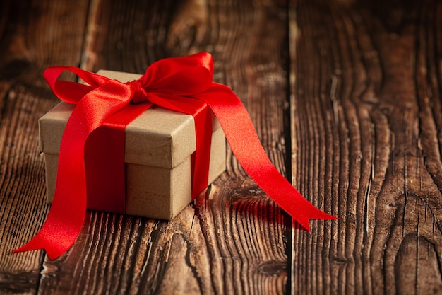 Caja de regalo con lazo de cinta roja sobre fondo de madera