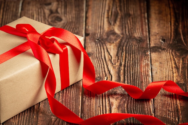 Caja de regalo con lazo de cinta roja sobre fondo de madera