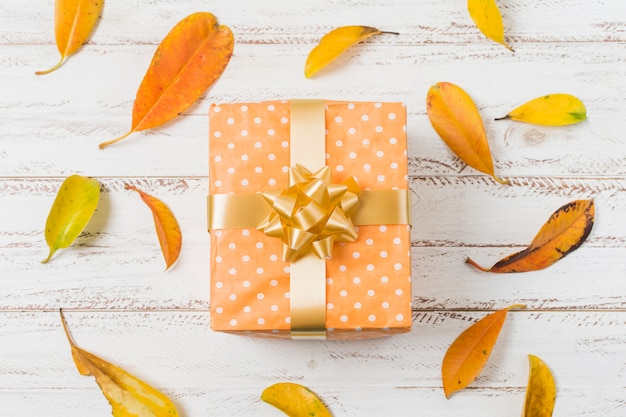 Caja de regalo con lazo y hojas de otoño sobre superficie de madera.