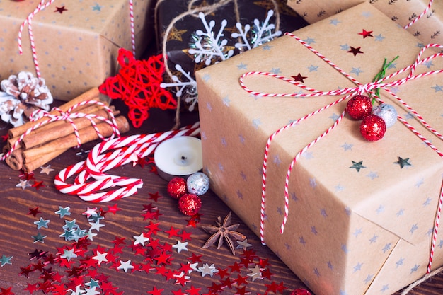 Caja de regalo navideña en una mesa festiva decorada con piñas, canela, caramelo, nueces y estrellas de destellos sobre fondo de madera