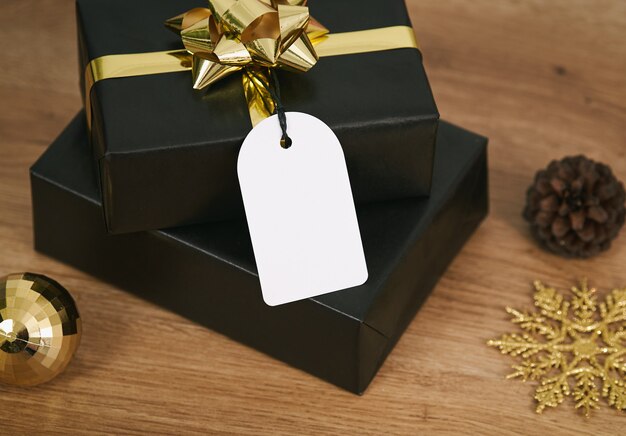 Caja de regalo negra y etiquetas de felicitación navideña de maqueta sobre fondo de mesa de madera