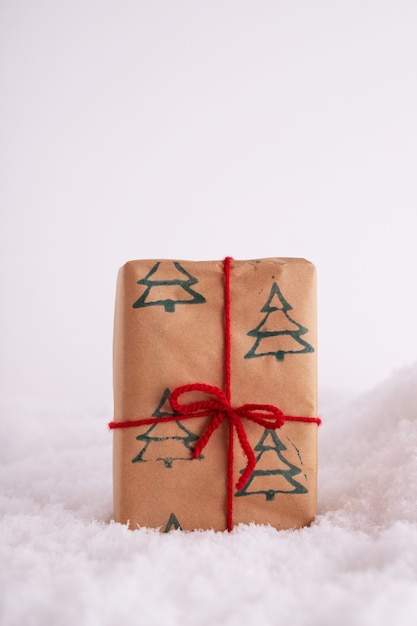 Caja de regalo con patrón de árboles de Navidad y una cinta roja en la nieve.