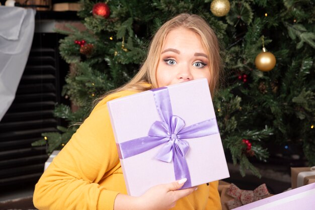 Caja de regalo púrpura de mujer joven en su mano sentada en el piso.