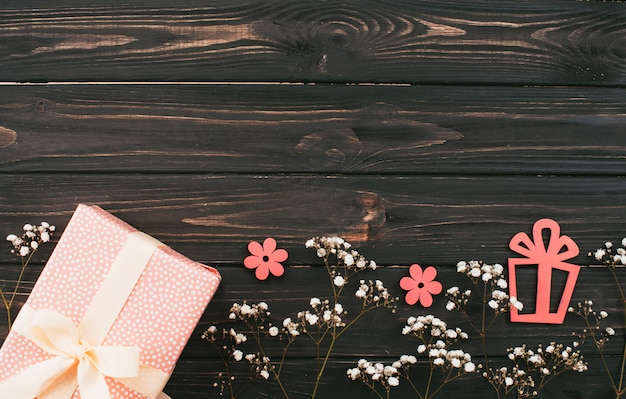 Caja de regalo con ramas de flores en mesa de madera.