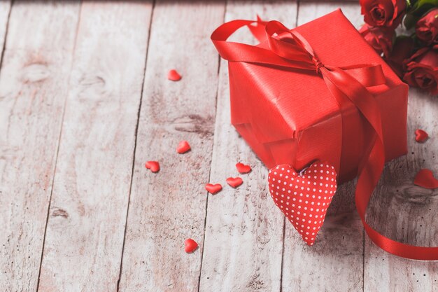 Caja de regalo roja sobre una mesa de madera con un corazón al lado