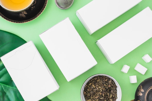 Cajas blancas con té saludable con hierbas y terrones de azúcar sobre fondo verde
