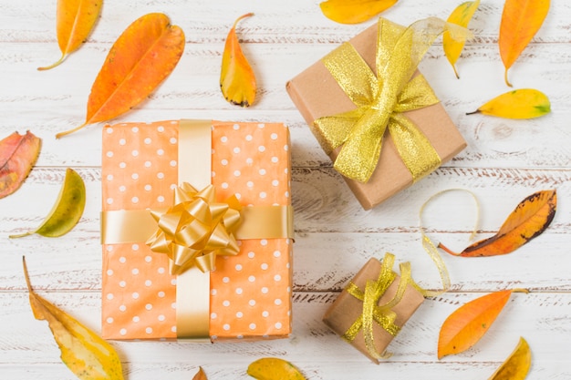 Cajas de regalo decorativas rodeadas de hojas de naranja en mesa blanca