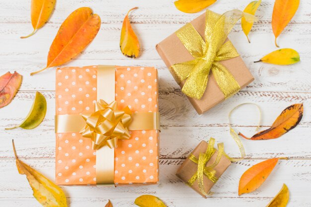 Cajas de regalo decorativas rodeadas de hojas de naranja en mesa blanca