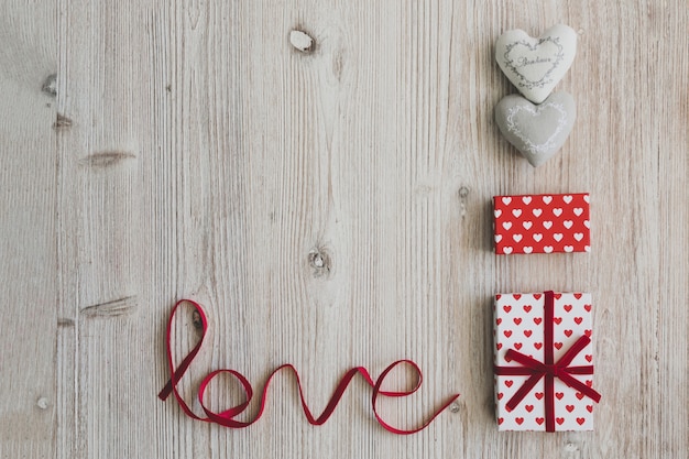 Cajas de regalo, dos corazones y la palabra "love" sobre una mesa de madera