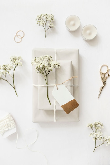 Cajas de regalo envueltas con flores de aliento de bebé y etiqueta con velas; tijera y anillos de boda