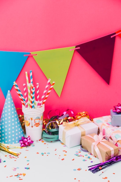 Foto gratuita cajas de regalo envueltas; sombrero de fiesta; serpentinas cinta arcos y empavesados contra fondo rosa