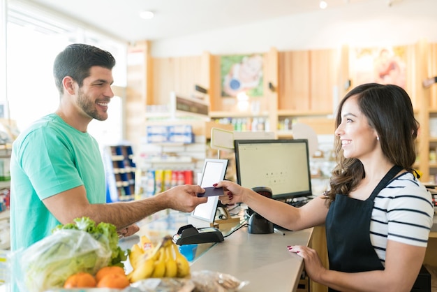 Cajera sonriente con el comprador en el mostrador de pago en la tienda de comestibles