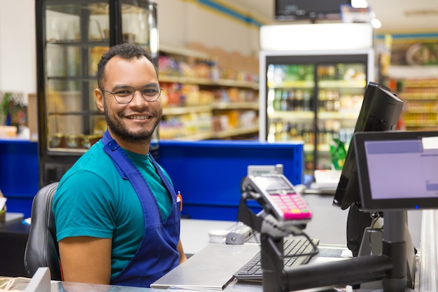 Cajero afroamericano sonriente sentado en la caja