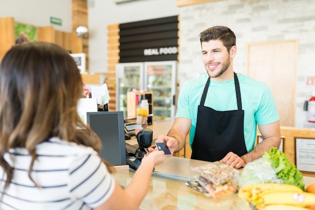 Foto gratuita cajero masculino sonriente que recibe el pago con tarjeta de crédito en el supermercado